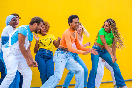 Multi-ethnic young friends dancing a choreography together in the street next to a yellow background