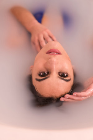 Artistic portrait of a woman lying in a bath half in water filled with milk