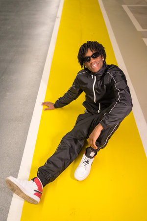 Vertical photo of an African modern musician sitting on the ground in an urban spaceの写真素材