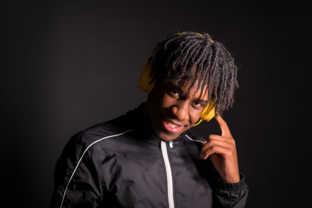 Dark studio portrait of a cool afro man listening music with headphones and looking at camera