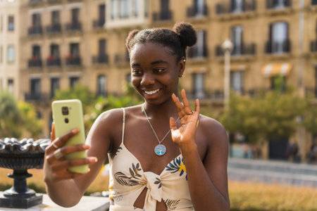 Young cute african woman waving during a video call with the mobile phone in the streetの写真素材