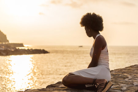 Tranquil scene of an afro woman gazing the ocean during sunsetの写真素材