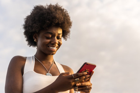 Low angle view portrait of an african woman using phone outdoors during sunsetの写真素材