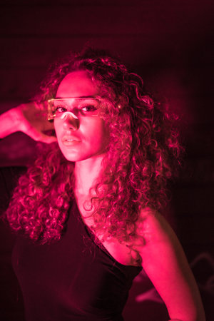 Vertical close-up portrait with pink neon lights of a sensual young woman with curly hair wearing smart glassesの写真素材