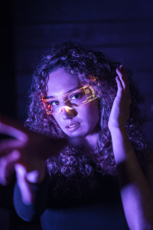 Vertical close-up portrait with purple neon lights of a sensual woman with smart glasses gesturing in an urban spaceの写真素材