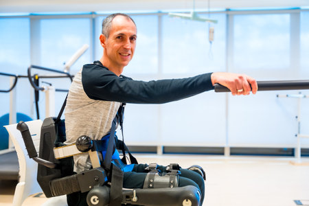 Mechanical exoskeleton. Portrait of disabled person with robotic skeleton in rehabilitation trying to get up alone, Physiotherapy in modern hospitalの写真素材