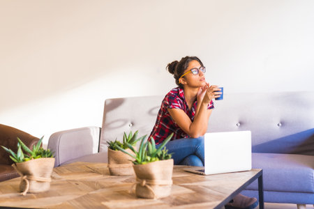 Horizontal photo of a young woman drinking coffee while working at homeの写真素材