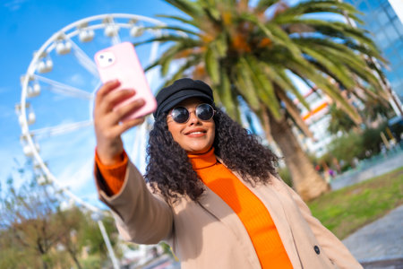 Chic tourist taking a selfie in the city enjoying sun in a winter dayの写真素材