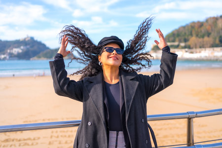 Chic latin woman in winter clothes arranging her hair in a beach view point