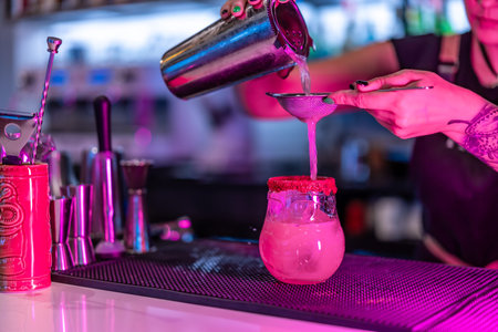 Cropped close-up photo of a woman mixing ingredients of a cocktail at the counter of a nightclub
