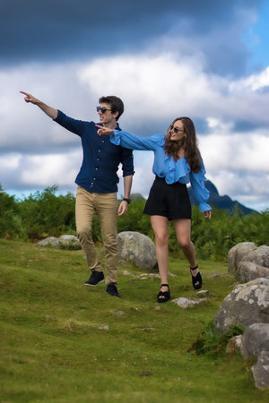 Vertical photo of a couple pointing to the horizon from a path in the mountain