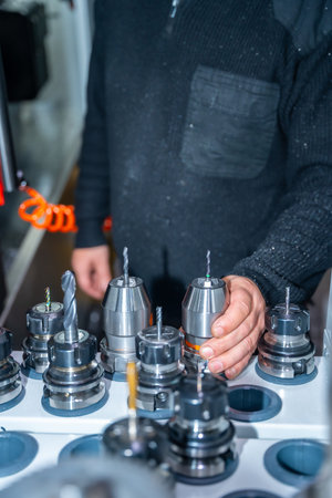 Vertical photo of an unrecognizable worker holding one lathe among a collection of lathes in a cnc...