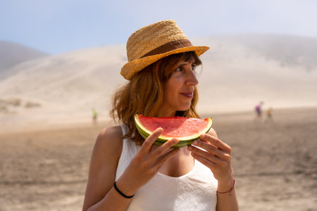 Woman eating a watermelon standing on a sandy bay in Cabo de Gata, Spainの写真素材