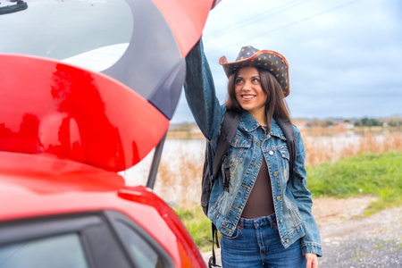 Portrait of a happy female adventurer traveling with red car on a road trip