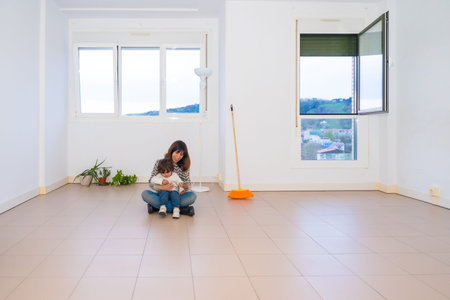 Mother and child sitting in the middle of an empty house after movingの写真素材