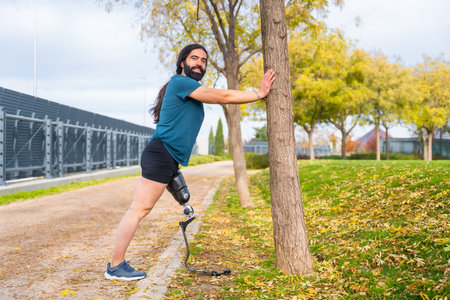 Happy disabled man with prosthetic leg stretching in a park after runningの写真素材