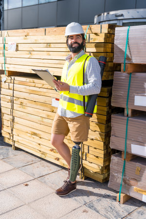 Vertical portrait of a smiley engineer with leg amputee working in a construction site