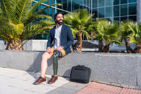 Businessman with prosthetic leg sitting outside a financial building in a sunny day in the cityの写真素材