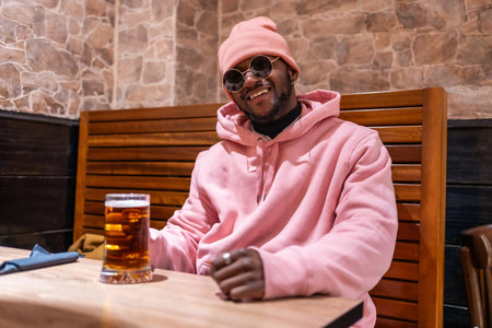 Portrait of a smiling cool african man in a bar drinking beerの写真素材