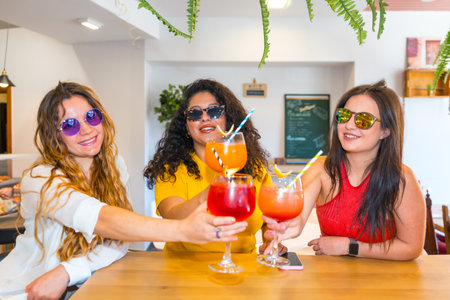 Frontal view of three cheerful women in sunglasses celebrating summer with friends toasting in a barの写真素材