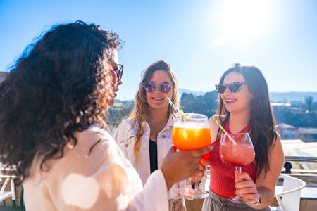 Three cool female friends enjoying summer toasting with cocktails on a rooftop in a sunny dayの写真素材