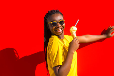 Urban scene of a happy girl eating ice cream next to a red wallの写真素材