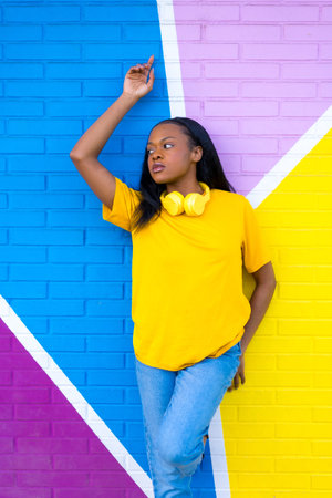 Vertical portrait of an african young woman posing standing and looking aside on a colorful wall