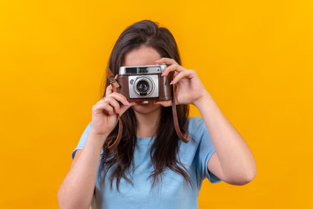 Studio portrait with yellow background of a casual young woman using an old fashioned camera