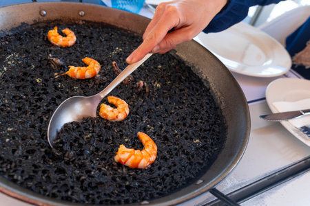 A spoon serving black rice with prawns and squid, a dry rice, cooked in paella or in a clay pot, a characteristic flavor of Valencian Mediterranean cuisine. Spainの写真素材