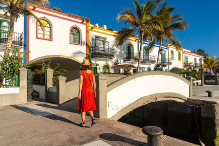 A tourist woman in a red dress walking in the port of the town Mogan in Gran Canaria in summerの写真素材