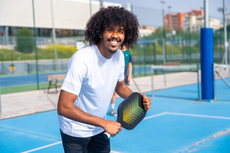 Portrait of a man with afro hairstyle smiling at camera having fun playing pickleball outdoorsの写真素材