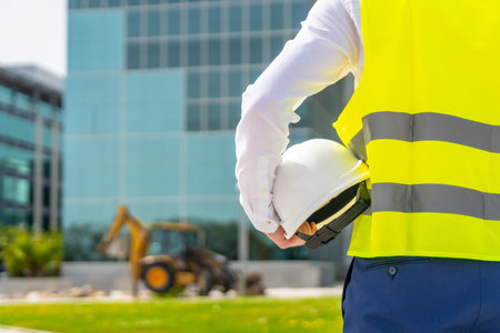 Rear view of an unrecognizable architect holding a helmet observing remodeling works in a financial...