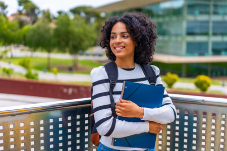 Latin female student smiling standing outside the campus of the university holding folder and...