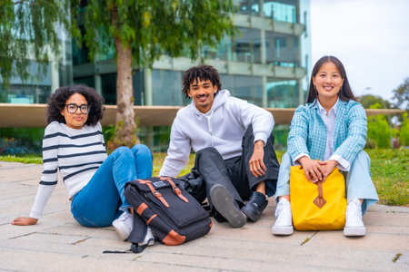 Portrait of three diverse cool university students sitting outside the campus