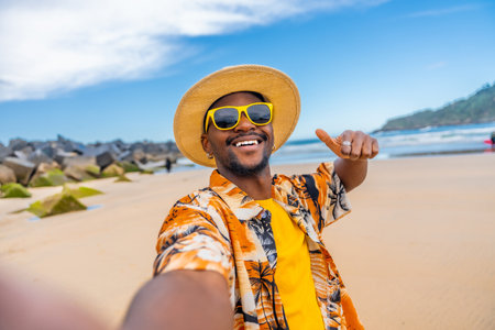African smiling man taking selfie gesturing with thumb up in a sandy beachの写真素材