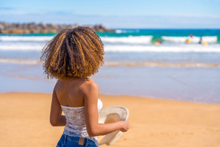 Rear view of a latin young fit woman with curly hair standing gazing the seaの写真素材