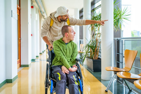 Caucasian young man showing something outside the university to a disabled friend sitting on...
