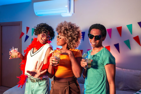 Multiracial friends drinking and dancing at home at night with colorful neon light illuminating the...