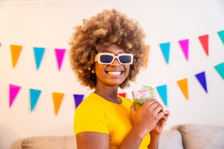 African woman with sunglasses holding a cocktail next to garlands decorating the house
