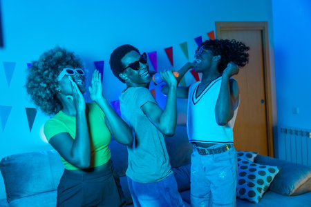 Friends singing and dancing karaoke at night with blue neon light illuminating the living roomの写真素材