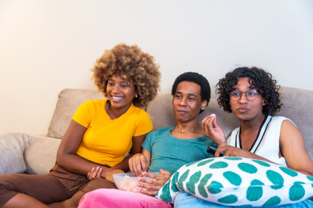 Multi-ethnic friends watching movie and eating popcorn sitting on the sofa at homeの写真素材