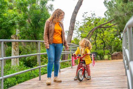 Caucasian adult mother supporting a child learning to ride a pink bike on a parkの写真素材