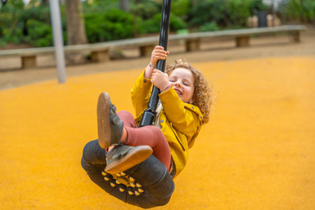 Little blonde caucasian girl with curly hair and colorful spring clothes enjoying swinging in a...
