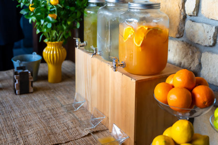 A table with a wooden stand holding pitchers of orange juice and lemonade. There are also oranges and lemons on the tableの写真素材