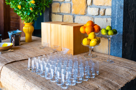 A table with a vase of oranges and lemons, and a box of oranges. The table is covered with glasses...