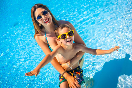 Happy family of a caucasian mother and boy having fun together inside a swimming pool in summerの写真素材