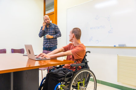 Caucasian man with disability and a work colleague working using laptop during a creative process in...