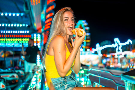Sensual blonde woman biting into a hot dog at night fairの写真素材