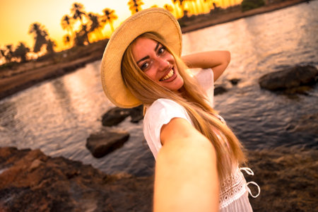 Personal point of view of a woman with sun hat taking a selfie during sunset on a tropical beachの写真素材