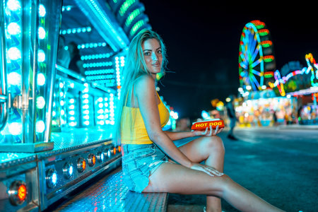 Side view photo of a woman at a night fair about to eat a hot dogの写真素材